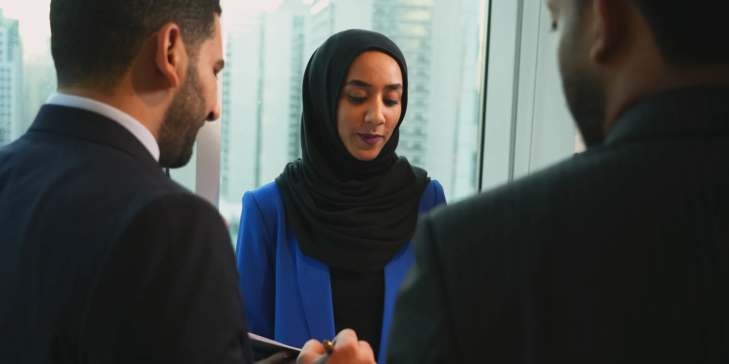 امرأة بسترة زرقاء وحجاب أسود تتحدث مع زميلين